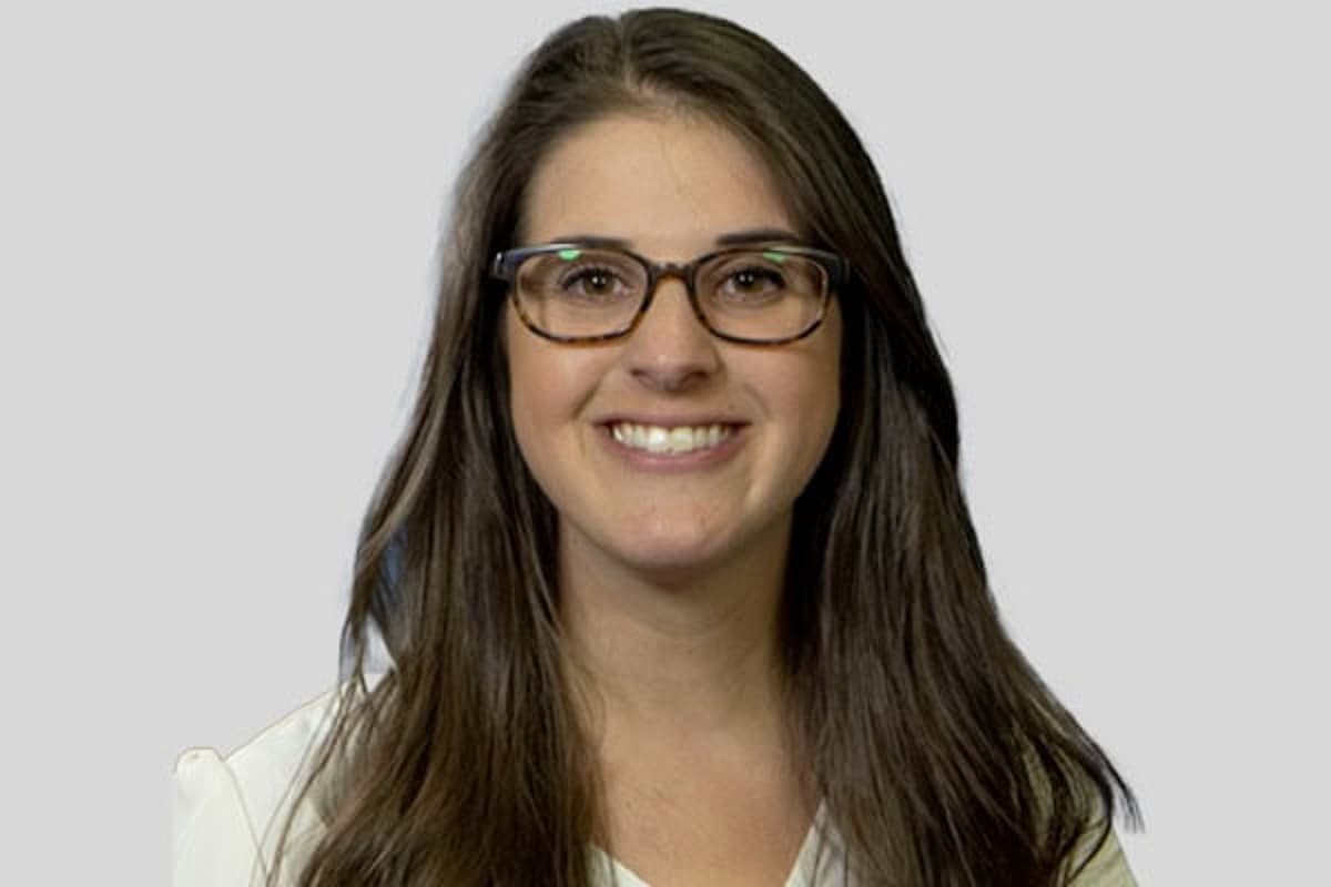 A woman with long brown hair, glasses, smiling