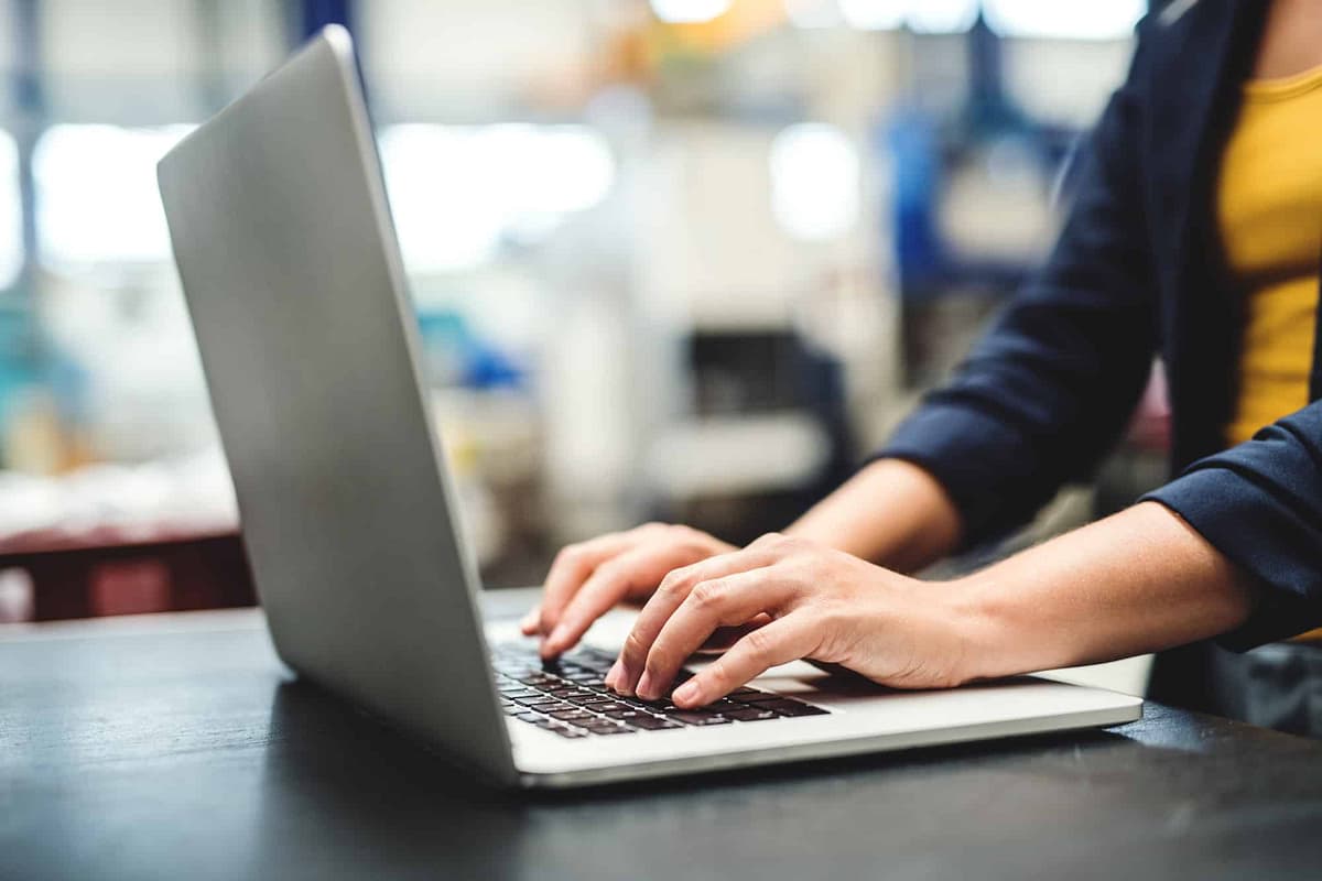 Person types on keyboard while using laptop at desk