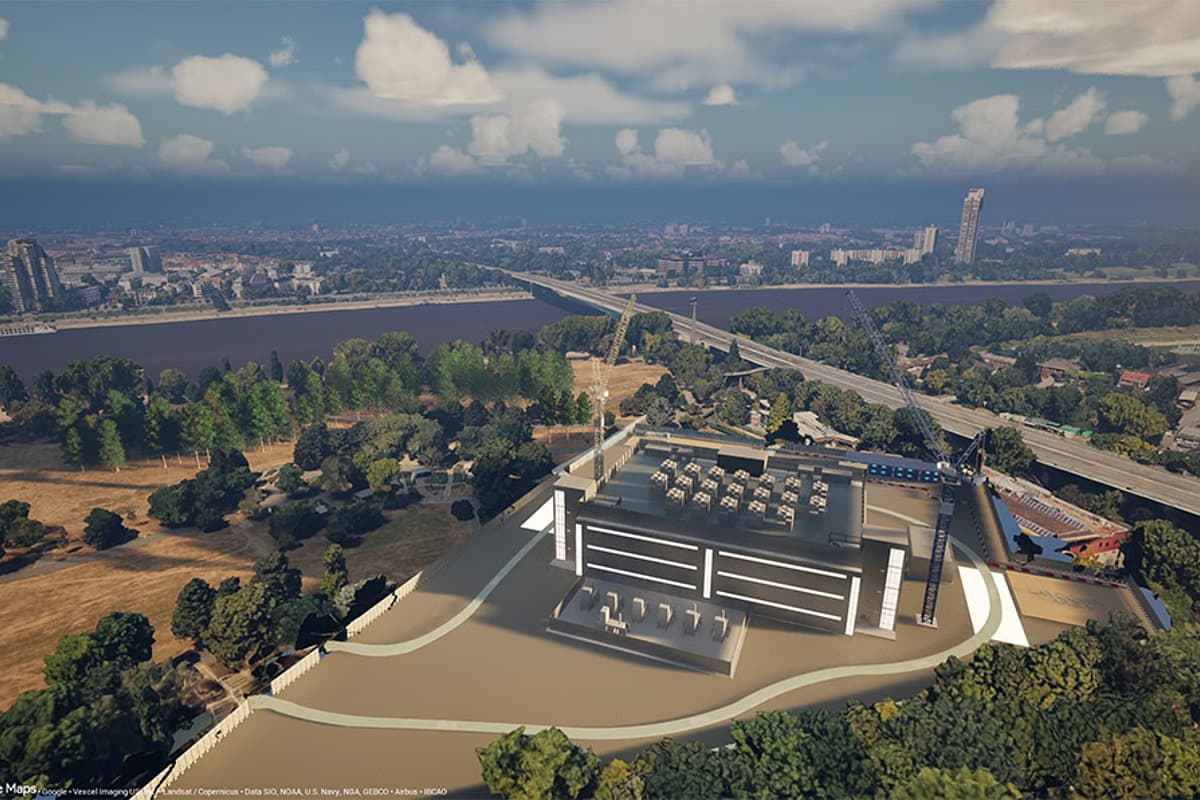 Aerial view of a modern stadium complex beside a wide river, surrounded by trees, highways, and a distant city under partly cloudy skies.