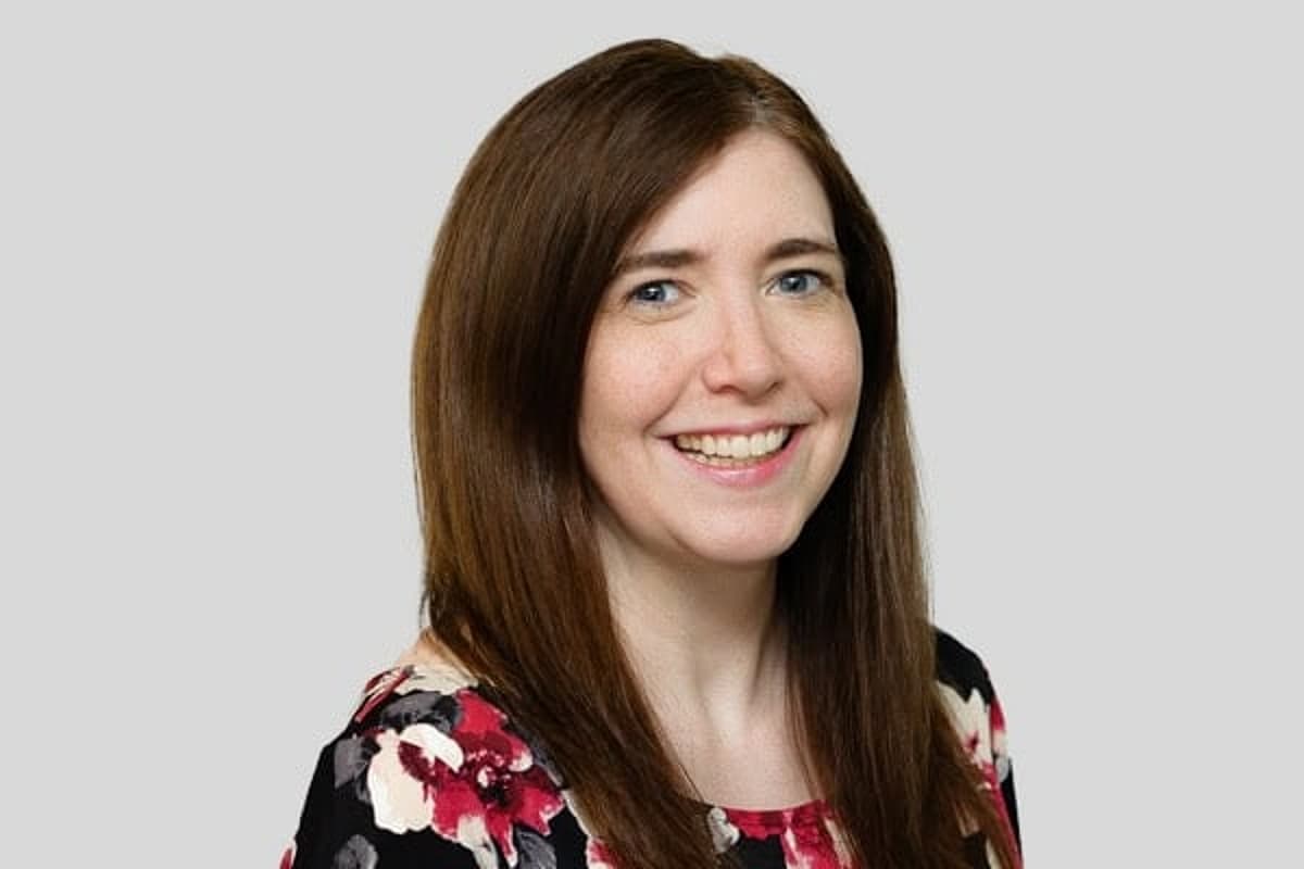 Woman with long brown hair and multicolored floral shirt smiling.