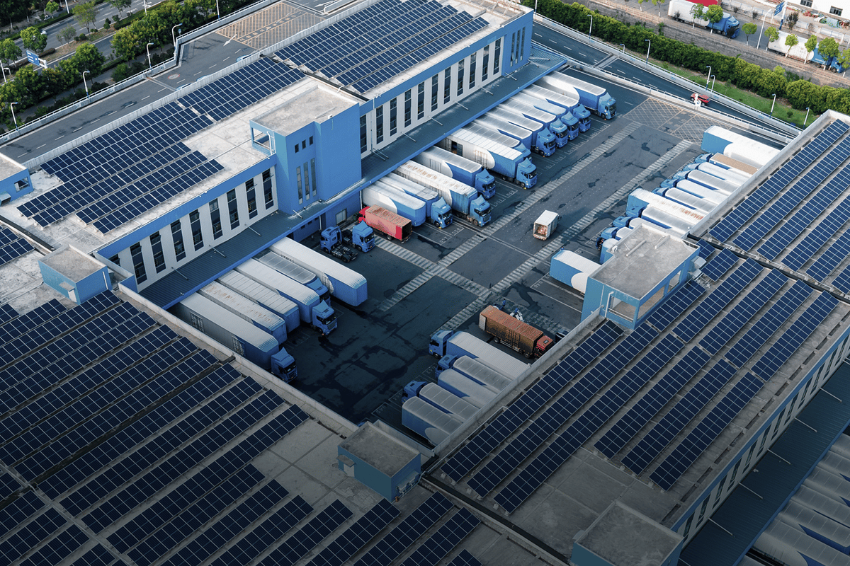 An aerial view of a modern logistics facility with solar-paneled roofs and docked cargo trucks, illustrating green industrial infrastructure and efficient commercial asset management.