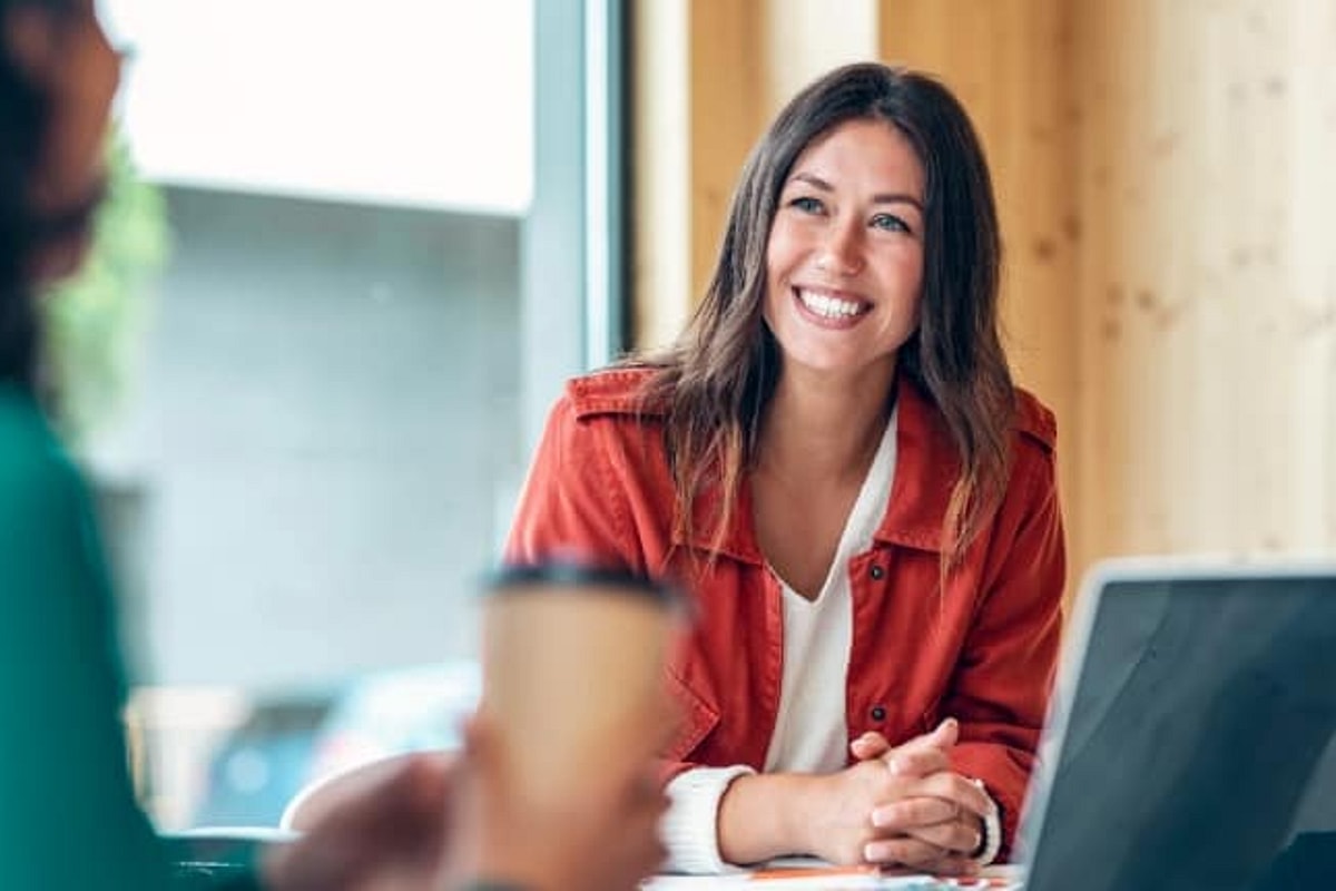 Woman with long hair smiles while conversing with another person who is off camera