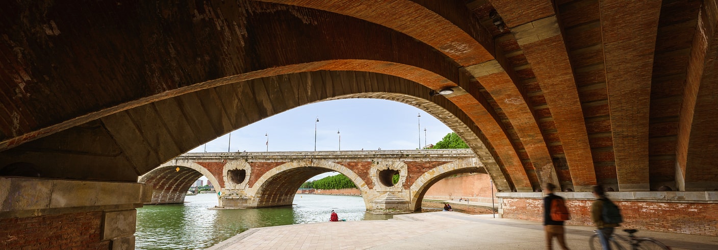 Man walks under a bridge overpass near body of water and adjacent bridge