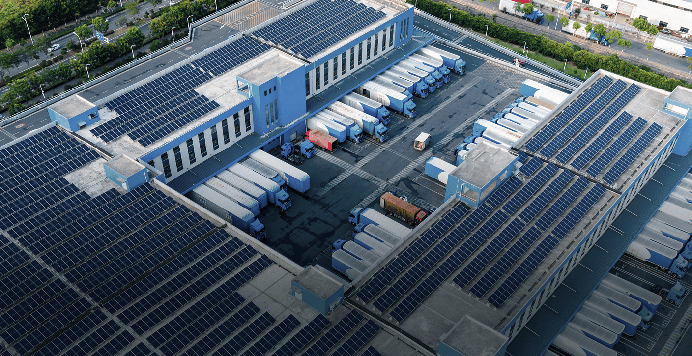 An aerial view of a modern logistics facility with solar-paneled roofs and docked cargo trucks, illustrating green industrial infrastructure and efficient commercial asset management.