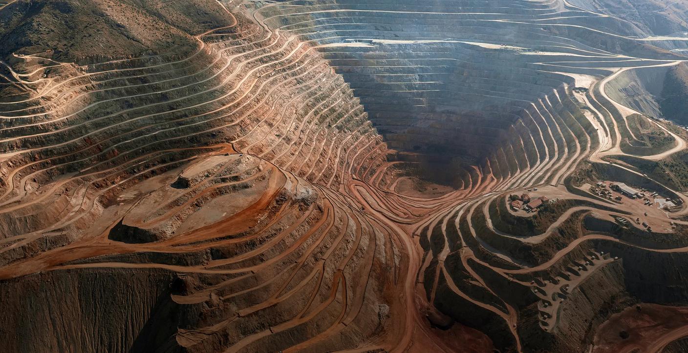 An aerial view of a massive, terraced open-pit mine carved into a mountain, highlighting large-scale excavation, resource recovery, and civil engineering in the mining sector.