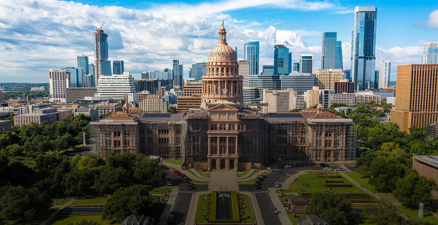 A sweeping skyline view featuring the historic Texas State Capitol building in Austin, framed by modern high-rise office towers, representing urban planning, historic preservation, and civic coordination.