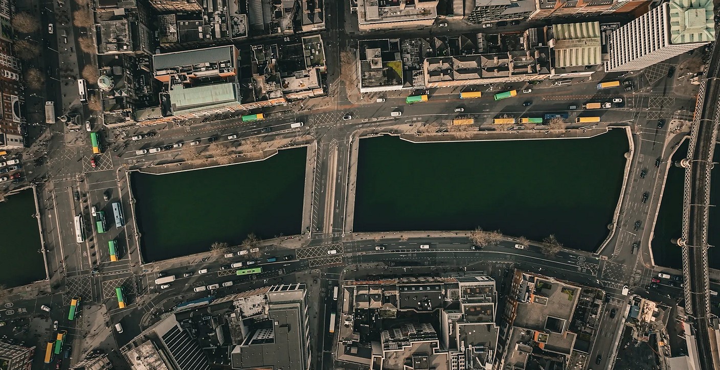 An aerial top-down view of an urban roundabout featuring a green central island, structured traffic lanes, red bicycle lanes, and pedestrian crosswalks, highlighting smart city design and urban mobility planning.