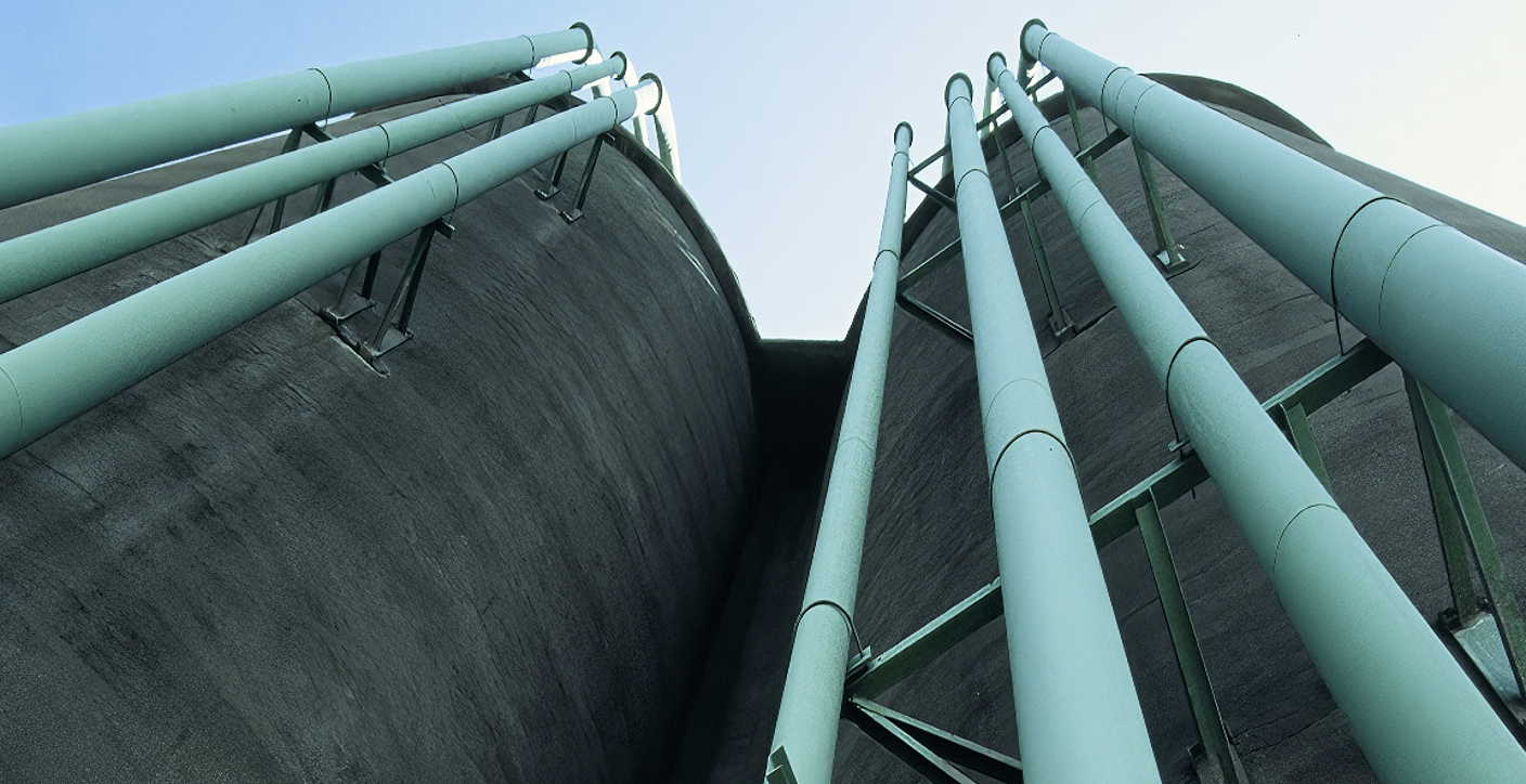Low-angle perspective of large concrete storage silos with industrial piping, highlighting robust municipal water distribution and treatment infrastructure.