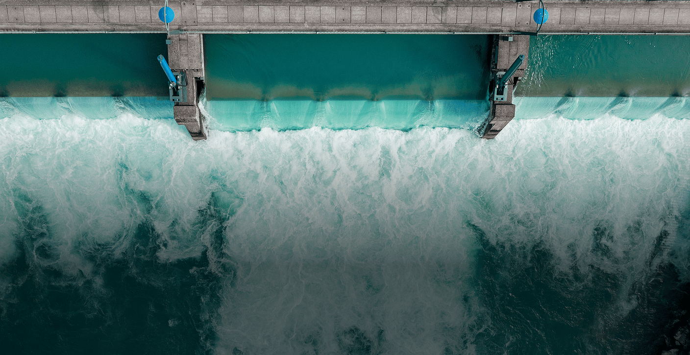 Top-down aerial view of open spillway gates releasing a powerful torrent of turquoise water, demonstrating active water resource management and renewable hydroelectric infrastructure.