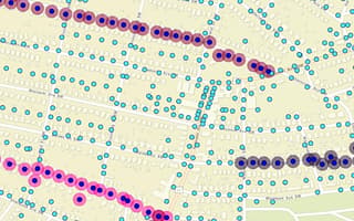 A GIS geographic map showing street grids of an urban area populated with blue, red, pink, and gray circular icons representing utility pole assets and lines in SPIDAstudio, demonstrating utility asset management.