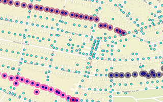 A GIS geographic map showing street grids of an urban area populated with blue, red, pink, and gray circular icons representing utility pole assets and lines in SPIDAstudio, demonstrating utility asset management.