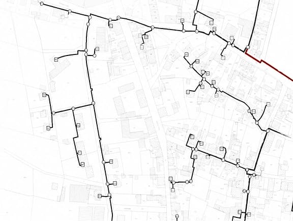 Municipal thermal or gas distribution network model in OpenUtilities sisHYD, showing building parcels, piping main routes, and system nodes on a technical grid map.
