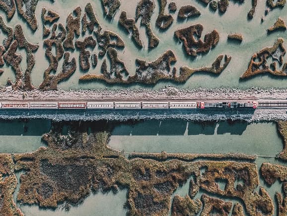 Aerial view of a cargo train traveling along a straight railway track through a scenic coastal wetland, highlighting sustainable freight transit and resilient rail infrastructure.