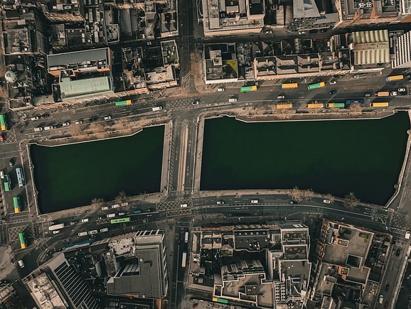 An aerial top-down view of an urban roundabout featuring a green central island, structured traffic lanes, red bicycle lanes, and pedestrian crosswalks, highlighting smart city design and urban mobility planning.