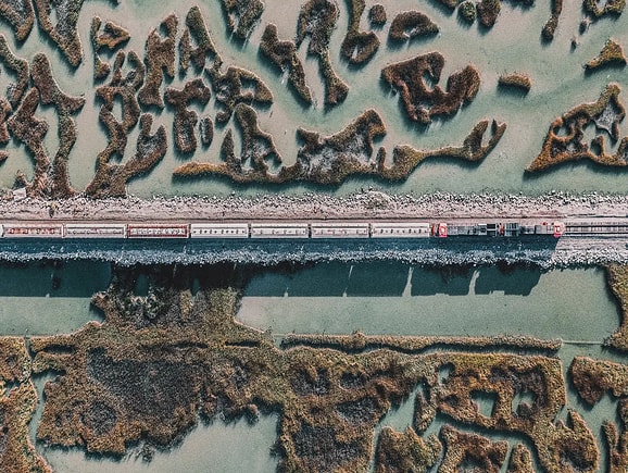 Aerial view of a cargo train traveling along a straight railway track through a scenic coastal wetland, highlighting sustainable freight transit and resilient rail infrastructure.