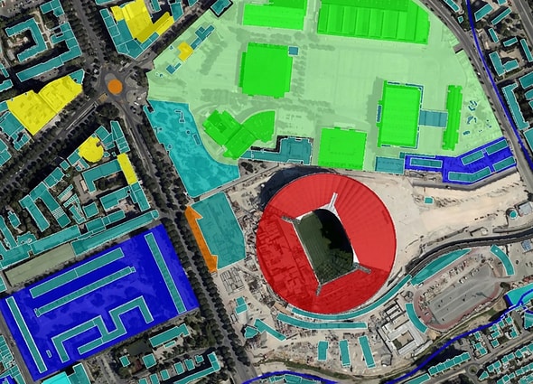 A top-down GIS map view in OpenCities Map featuring a stadium with a red circular roof, surrounded by green, blue, and yellow color-coded building plots for urban planning.