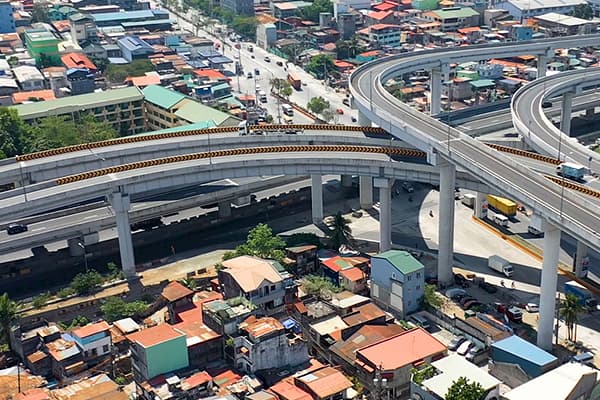 Aerial view of elevated rail tracks and looping highways above a dense neighborhood of colorful homes, conveying urban growth and stark contrasts.