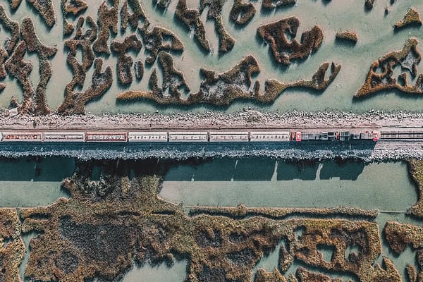 Aerial view of a cargo train traveling along a straight railway track through a scenic coastal wetland, highlighting sustainable freight transit and resilient rail infrastructure.