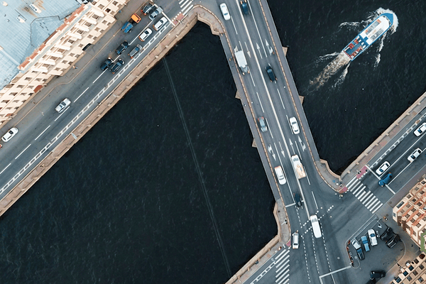 An aerial view of an active multi-lane roadway bridge crossing a river with a passenger boat traveling below, illustrating civil engineering, public transportation, and connected urban infrastructure.