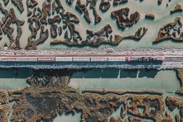 Aerial view of a cargo train traveling along a straight railway track through a scenic coastal wetland, highlighting sustainable freight transit and resilient rail infrastructure.
