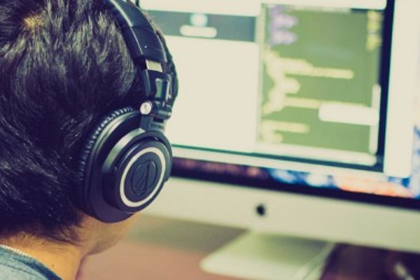 Man wearing headphones works at desk with computer monitors