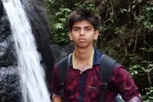 Man wearing red shirt and backpack poses in front of waterfall