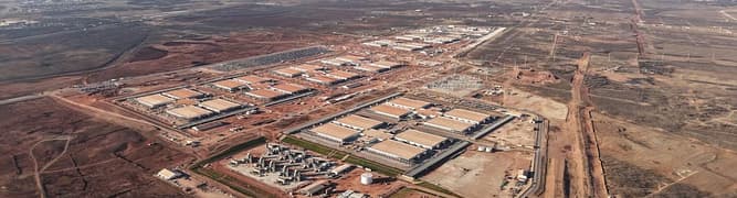 Aerial view of a large industrial complex with multiple buildings, surrounding infrastructure, and nearby construction by DPR Construction on a vast, mostly barren Texas landscape—ideal for hyperscale AI data centers.