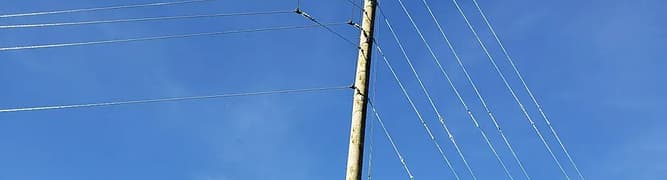 A wooden utility pole stands against a clear blue sky, its multiple power lines extending outward—a classic example of utility pole design that meets CSA compliance standards.