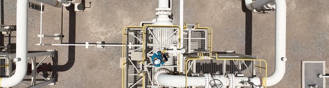 An aerial, top-down view of an engineer using a mobile tablet to conduct an inspection on a platform at an oil and gas facility, representing the move to digitalized, proactive asset management. 