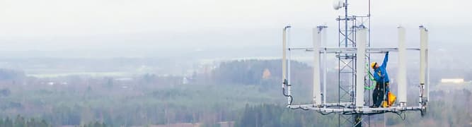 A technician in full safety gear works on a telecommunications tower, representing the physical 5G upgrades that Intrepid Group designs and analyzes using OpenTower.