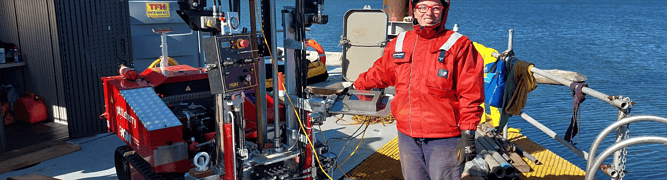 A pitt & sherry geotechnical engineer stands on a barge next to a red Pagani CPT rig during a nearshore ground investigation.