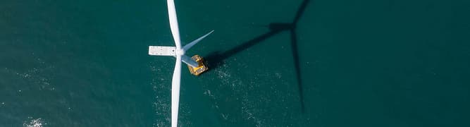 Aerial view of an offshore wind turbine with a maintenance vessel nearby, casting a long shadow across the water—ideal for integrating substation data to optimize operations and ensure efficient energy transmission.