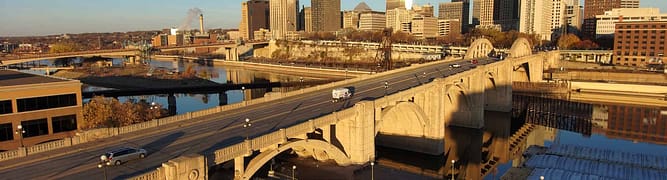 Aerial view of vehicles crossing the Robert Street Bridge, set against a backdrop of skyscrapers under a clear blue sky in St. Paul, Minnesota.