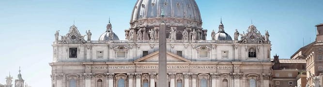 St. Peter's Basilica with a central obelisk in St. Peter's Square, Vatican City, under a clear blue sky.