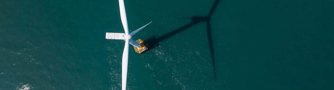 Aerial view of an offshore wind turbine with a maintenance vessel nearby, casting a long shadow across the water—ideal for integrating substation data to optimize operations and ensure efficient energy transmission.