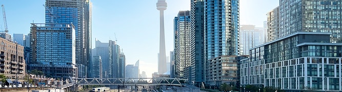 Downtown Toronto cityscape with train tracks and advanced rail protection in the foreground, modern high-rise buildings, and the CN Tower visible in the center background under a clear sky—showcasing Toronto rail safety innovators at work.