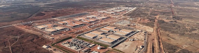 Aerial view of a large industrial complex with multiple buildings, surrounding infrastructure, and nearby construction by DPR Construction on a vast, mostly barren Texas landscape—ideal for hyperscale AI data centers.