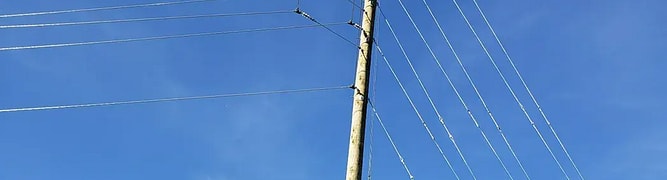 A wooden utility pole stands against a clear blue sky, its multiple power lines extending outward—a classic example of utility pole design that meets CSA compliance standards.
