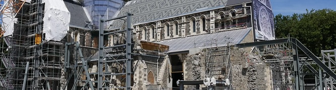 The historic Christ Church Cathedral undergoing major reconstruction, with large-scale scaffolding and construction equipment supporting the damaged stone walls.