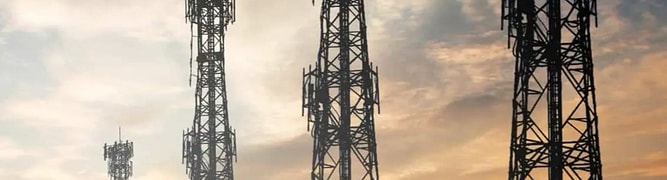 A telecommunications tower with multiple antennas and satellite dishes, overlooking a sprawling cityscape at dusk.