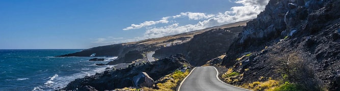A scenic, winding coastal highway in Hawaii, with the road running along a rocky shoreline next to the ocean 