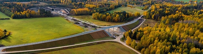 A section of the 211-kilometer greenfield railway designed by IDOM for the Rail Baltica project, showing a new overpass and earthworks amidst fields and forests.