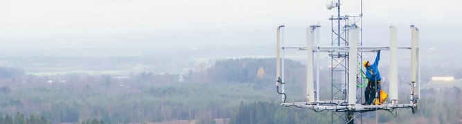 A technician in full safety gear works on a telecommunications tower, representing the physical 5G upgrades that Intrepid Group designs and analyzes using OpenTower. 