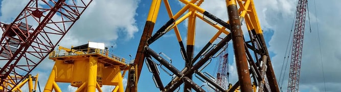 Yellow steel jacket foundations for an offshore wind farm being assembled on land with cranes 