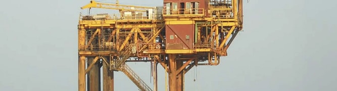 An aging yellow offshore oil and gas platform standing in the middle of the ocean 