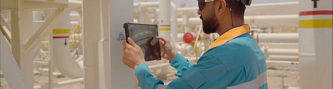 A field technician at an OQ Upstream industrial facility uses a mobile tablet to perform digitized inspections and check asset performance data.