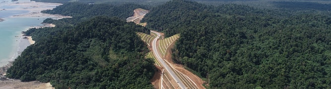 An aerial view of the Pan Borneo Highway Sarawak construction, cutting through the dense, hilly, and coastal landscape of Sarawak, Malaysia.