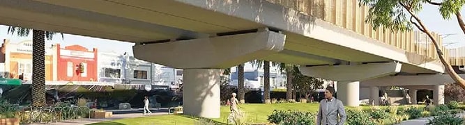 endering of a person walking under a modern elevated rail bridge in a landscaped urban park