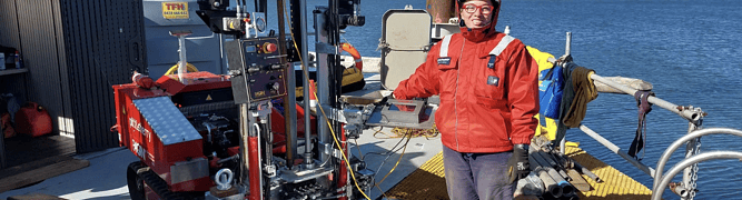 A Pitt & Sherry geotechnical engineer stands on a barge next to a red Pagani CPT rig during a nearshore ground investigation