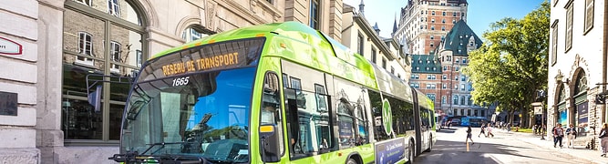 A bright green articulated bus from Quebec's Réseau de transport de la Capitale (RTC) operates on a street in historic Old Quebec, with the Château Frontenac visible in the background.